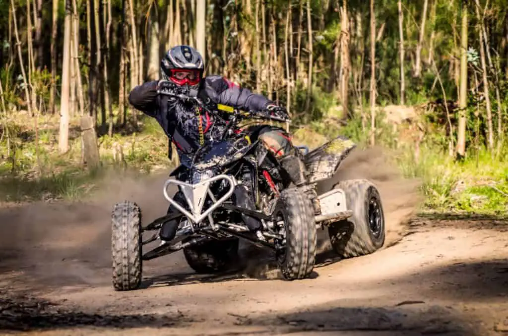 ATV racer takes a turn during a race on a dusty terrain