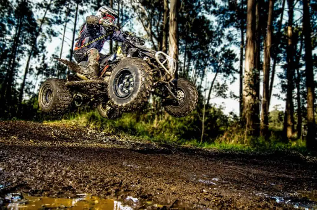 Quad rider jumping on a muddy forest trail
