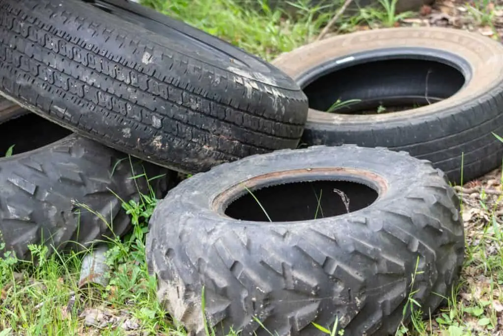 Pile of tires sitting in the grass and weeds