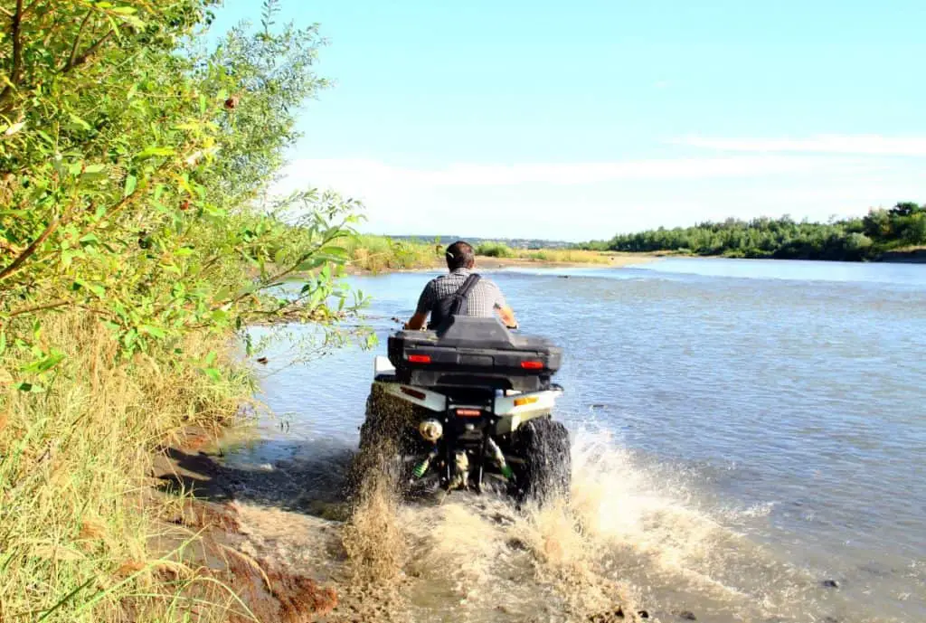 A man rides a White ATV with spray along the river