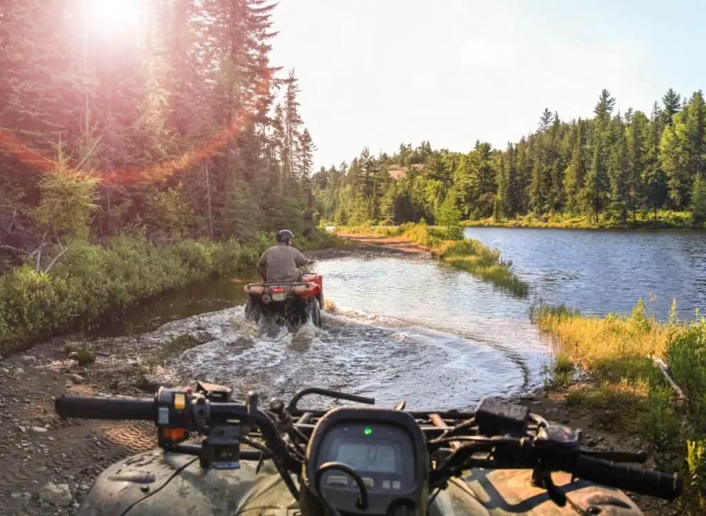 People driving ATV quads through water. Lake in Ontario, Canada.